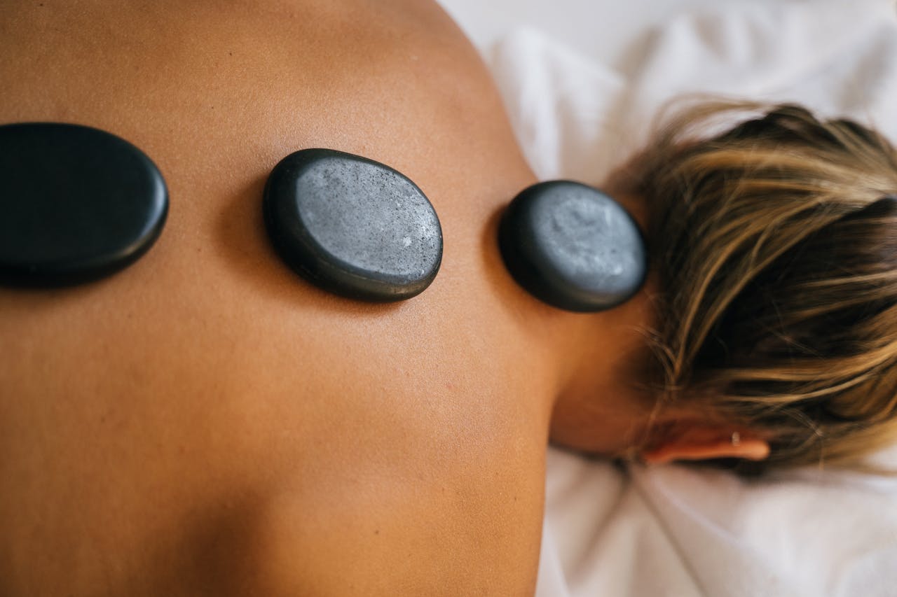 Close up photograph of pebbles on a the bare back of a woman laying face down on a massage table